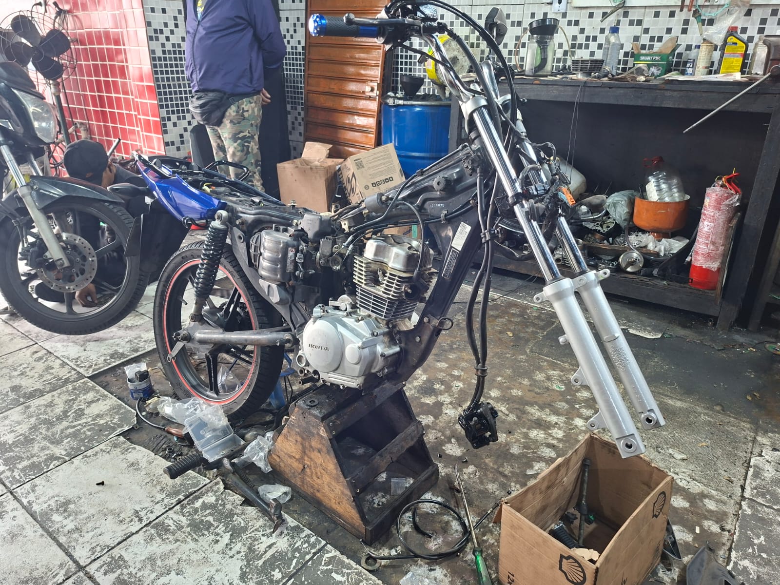 Honda CG desmontada na oficina, apenas chassi, motor e garfo